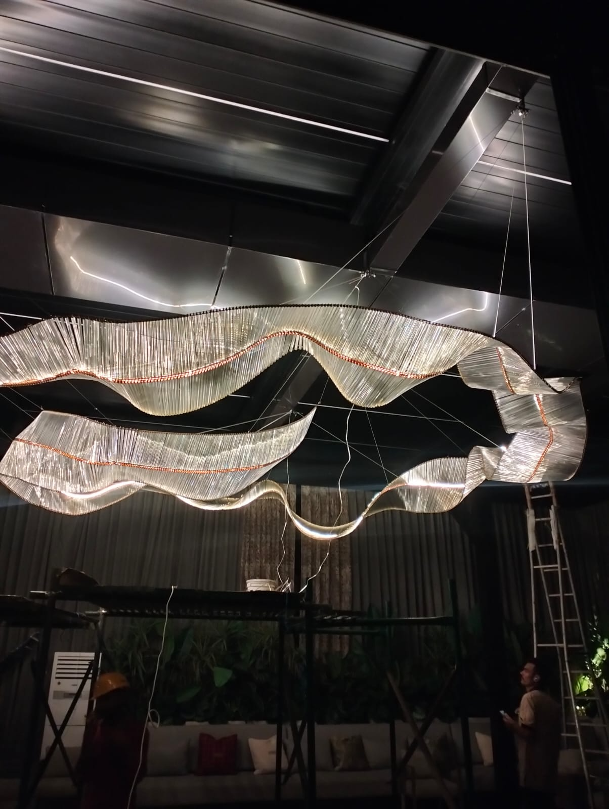 Large architectural ribbon chandelier professionally installed by luxury lighting specialists in India.